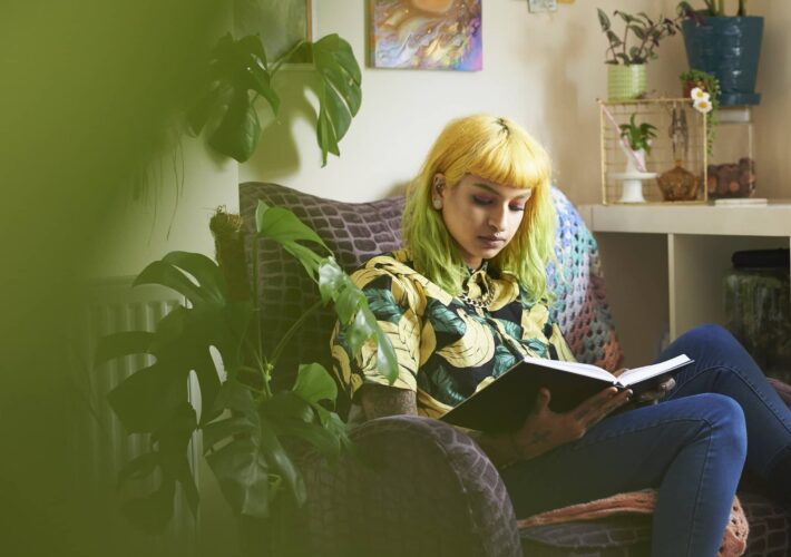 woman reading on couch sin room full of plants
