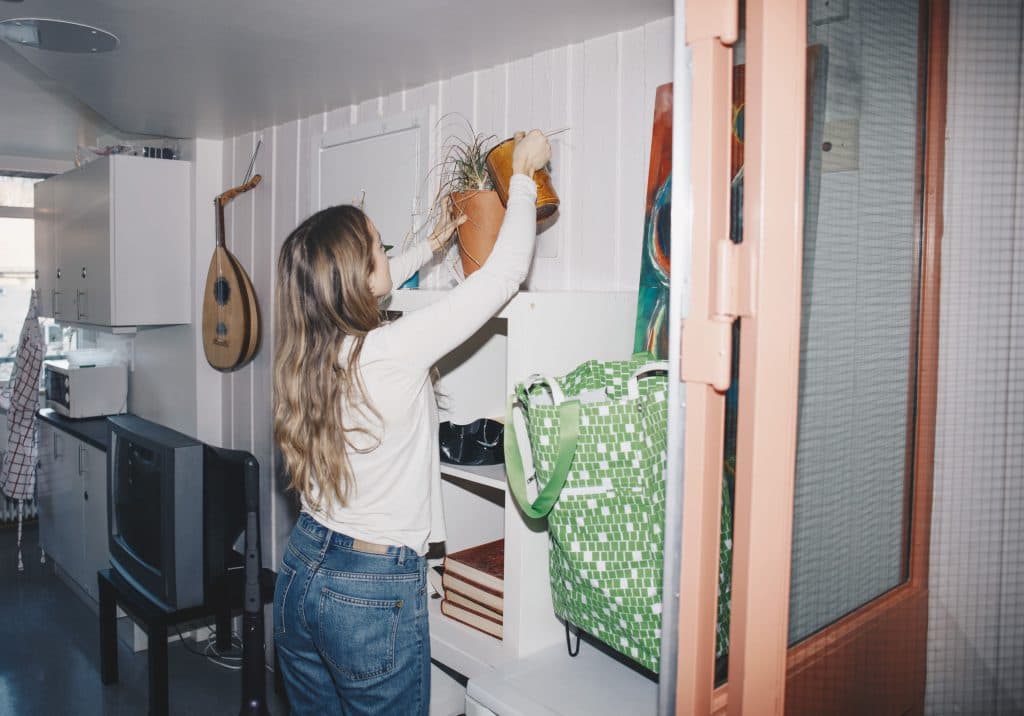 Girl watering her plants on top of a bookcase at home. For these spots, low maintenance varieties make decorating with plants easy.